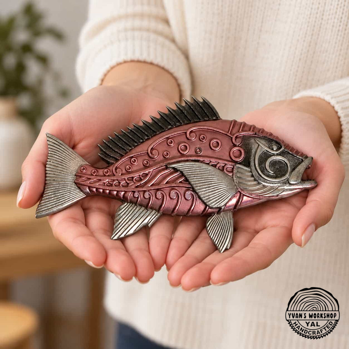 Silver and salmon metallic fish ornament held across two hands