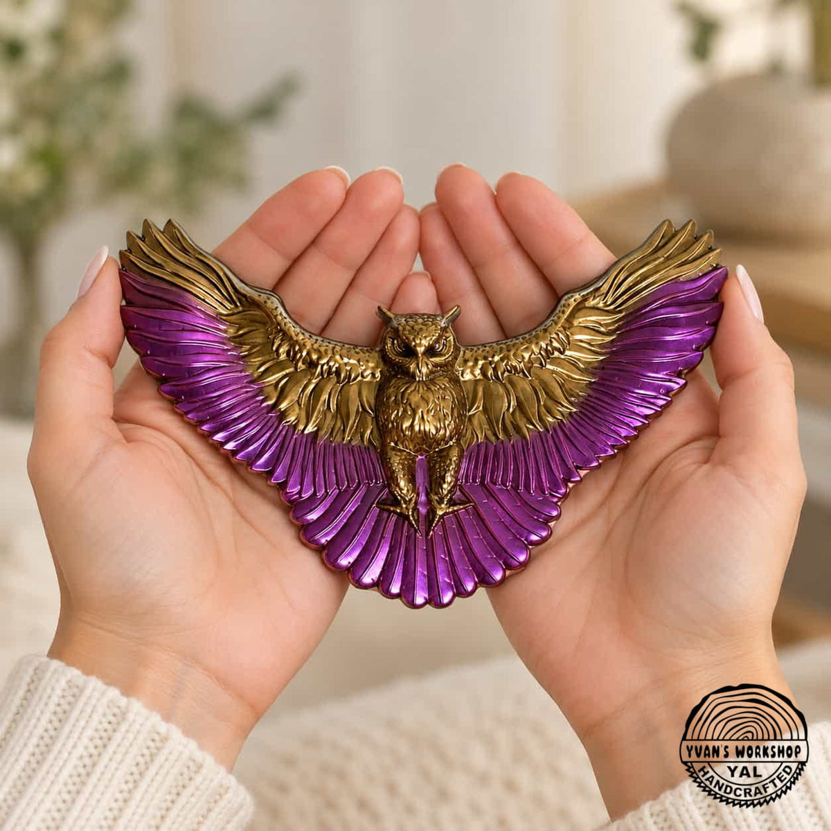Gold and purple spread-wing owl ornament held across two open hands